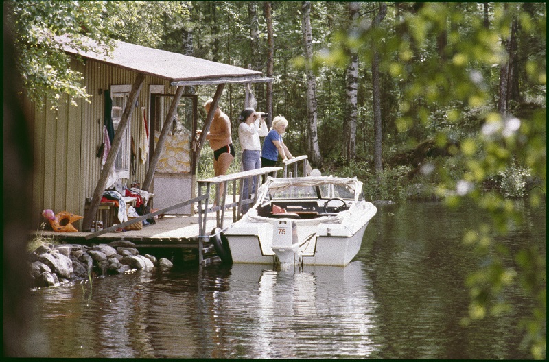 Mikonsaari, Aarne, A. 1982. Kesänviettoa veden äärellä; rantaviivalle rakennettu sauna tai mökki, vieressä moottorivene